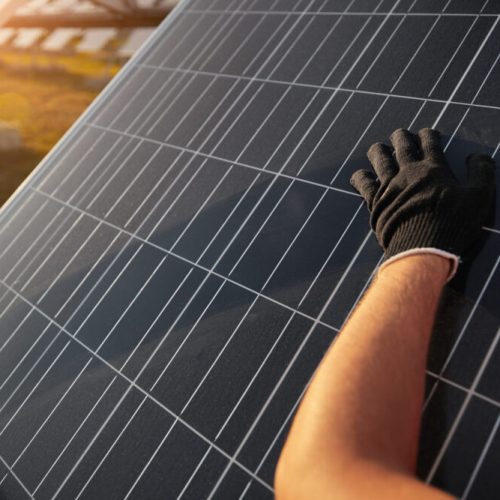 Crop anonymous workman in black glove wiping dusty photovoltaic panel during maintenance works on solar power station
